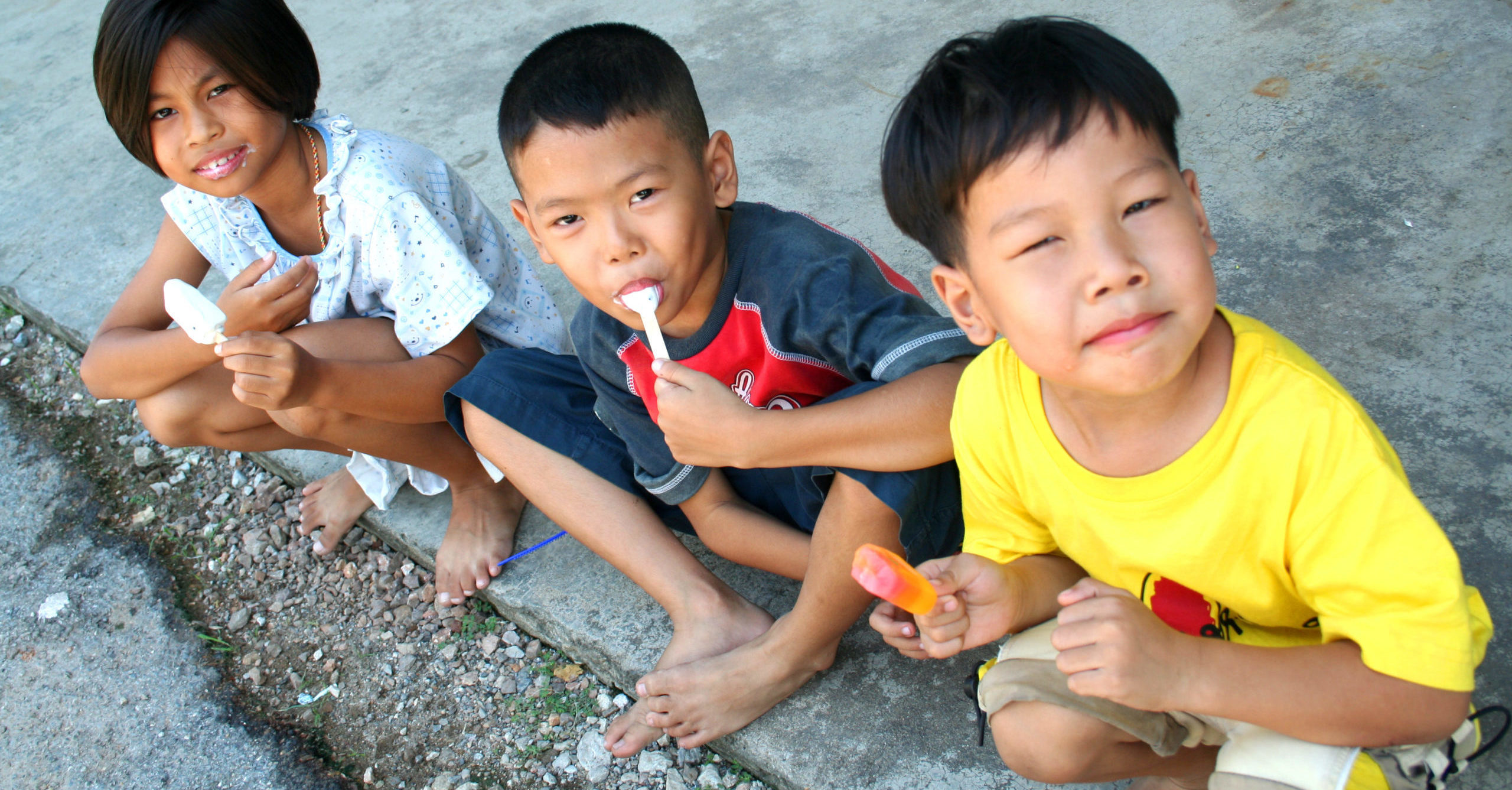 Three children eating Popsicles in the street